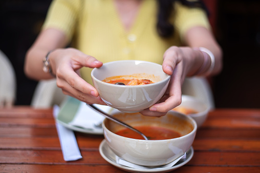 Woman having Thai Tom Yum Gong soup with seafood and vegetables in a restaurant closeup