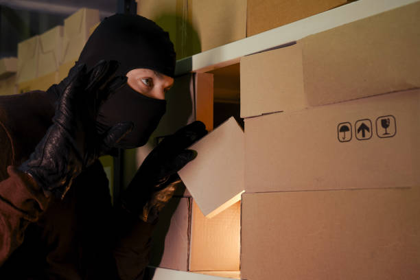 istock A thief wearing a ski mask picks up a box with a parcel from a warehouse at night 1285069779