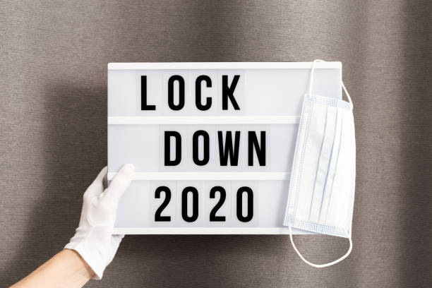 mãos em luvas brancas seguram caixa de luz com bloqueio de mensagens 2020 e máscara de proteção cirúrgica. a palavra do ano de 2020 está encerrada. - housebound - fotografias e filmes do acervo