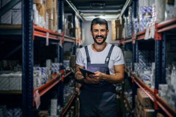 istock Smiling bearded tattooed hardworking employee holding tablet and standing in storage. 1285070912