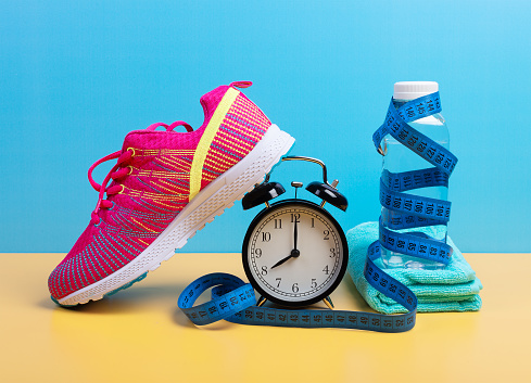Weight loss and training concept with measuring tape, bottle of water, towel and sneaker over blue wall background. Fitness and running equipment set