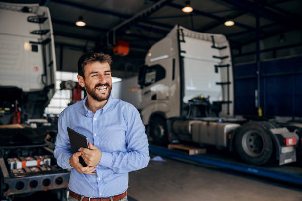 sorridente capo in piedi in auto park e in possesso di tablet. sullo sfondo ci sono i camion. impresa per l'importazione e l'esportazione. - mezzo di trasporto foto e immagini stock