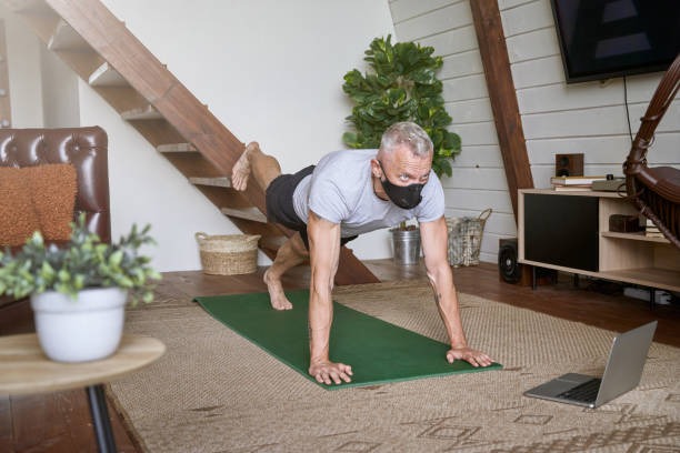 istock Exercising at home in self isolation. Middle aged man wearing face protective mask standing in plank pose in the living room while watching online workout on laptop 1285074359