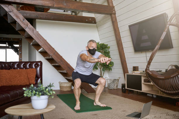 istock Staying active in self isolation. Middle aged athletic man wearing face protective mask exercising at home while watching online workout on laptop 1285074435
