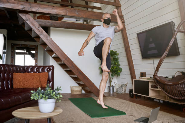istock Stay active during covid 19 outbreak. Sporty middle aged man wearing face protective mask exercising at home in self isolation while watching online workout on laptop 1285074474