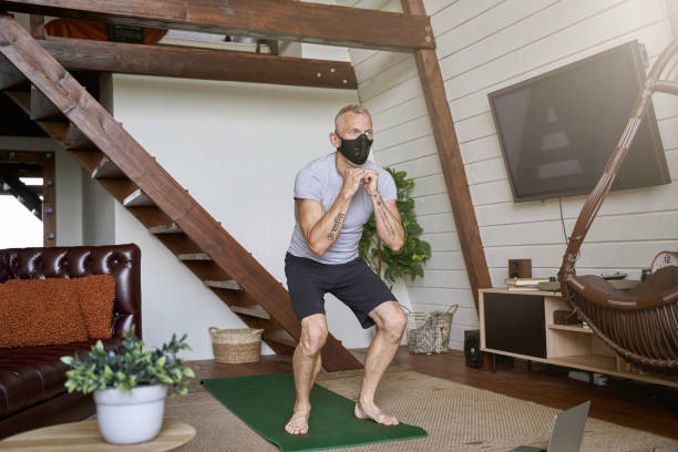 istock Staying fit during covid 19 outbreak. Sporty middle aged man wearing face protective mask exercising at home while watching online workout on laptop, full length shot 1285074570