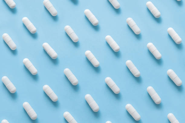 istock Scattered Pills on a blue background , Medicine concept. Multiple long white capsules on a blue. Pattern of capsules on a blue. 1285075386