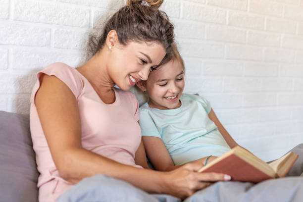 istock Mother and daughter in bed reading a book 1285076326