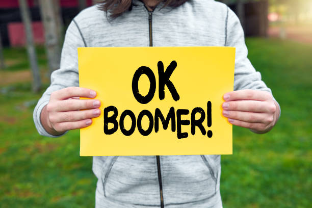 adolescente sostiene una pancarta con la palabra ok boomer contra el fondo de la naturaleza - diferencia entre generaciones fotografías e imágenes de stock