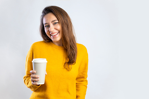 Smiling young woman drinking coffee from a paper cup on white background