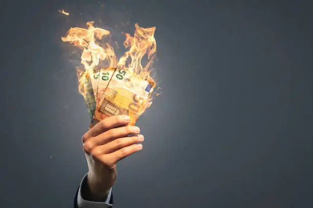 A hand of a businessman is holding several burning Euro banknotes. Copy space and neutral background.