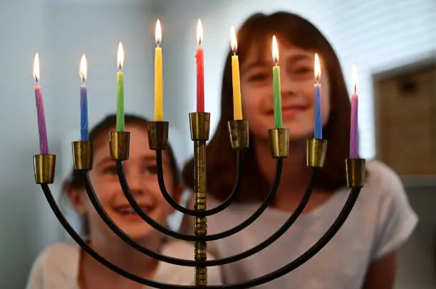 Two happy Jewish sisters looking and singing at a beautiful menorah candelabra glowing on the eight day of Hanukkah Jewish holiday.