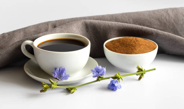 Cup with chicory drink, powder and blue flowers on white background. A useful coffee substitute. Side view.