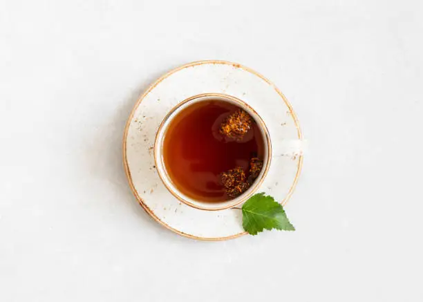 Photo of Chaga tea on a white background. Drink with pieces of birch mushroom in a white cup. View from above.