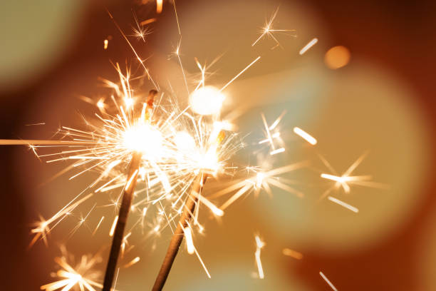 A pair of sparklers burn with a soft yellow light, scattering small stars of sparks around them A pair of sparklers burn with a soft yellow light, scattering small stars of sparks around them glittering burning stock pictures, royalty-free photos & images