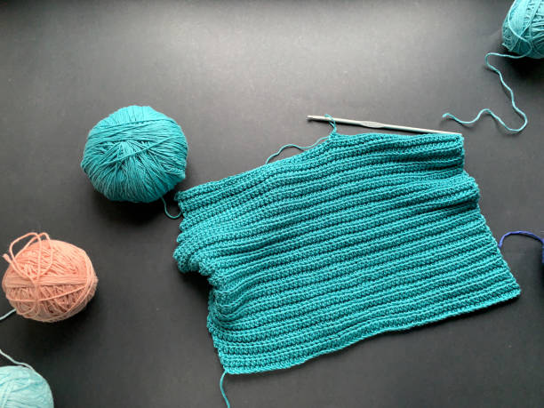 istock Crocheting process, turquoise thread on a black background. A skein of yarn and a crochet hook. The concept of creating a product with your own hands. Needlework, Hobbies. 1285092889
