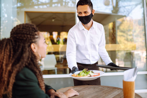 istock Young waiter in protective face mask and gloves with ordered meals, ready to serving guest. 1285093139