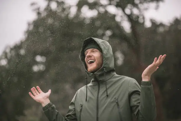 In the rain . Young man in a green coat standing in the rain and smiling