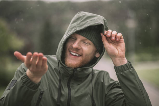 istock Man in a green coat catching rain drops and smiling 1285094763