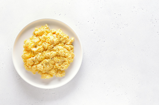Scrambled eggs on plate over white stone background with copy space. Top view, flat lay