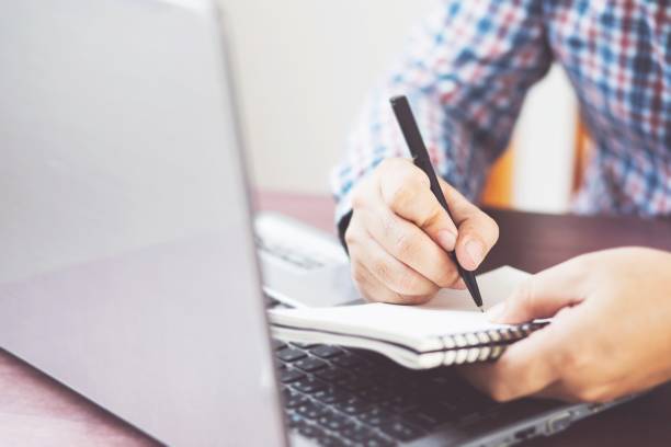 istock Young businessman sitting at a table at home working on a laptop and writing down ideas in a notebook 1285102430