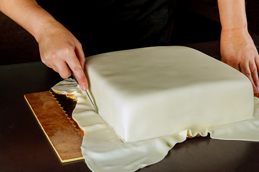 Woman in bakery covering wedding cake with white fondant.