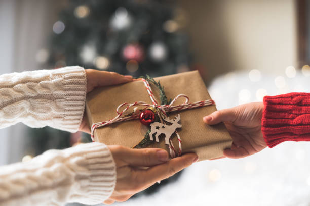 frau im pullover gibt ein gewickeltes weihnachtsgeschenk-box an kind. glühender schneebokeh, tannenbaum. winterferien - geschenk stock-fotos und bilder