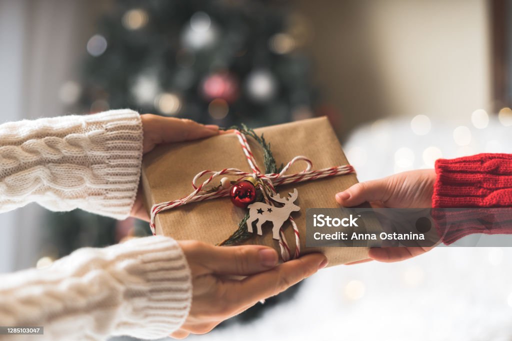 Woman in sweater giving a wrapped Christmas gift box to child. Glowing snow bokeh, fir tree. Winter holidays Woman in sweater giving a wrapped Christmas gift box to child. Glowing snow bokeh, fir tree. Winter holidays. Gift Stock Photo