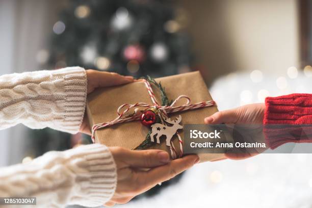 Woman In Sweater Giving A Wrapped Christmas Gift Box To Child Glowing Snow Bokeh Fir Tree Winter Holidays Stock Photo - Download Image Now