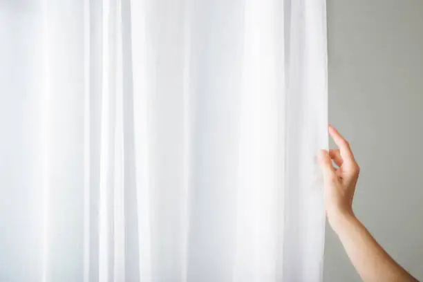 Young adult woman hand opening white day curtains at window. Closeup.