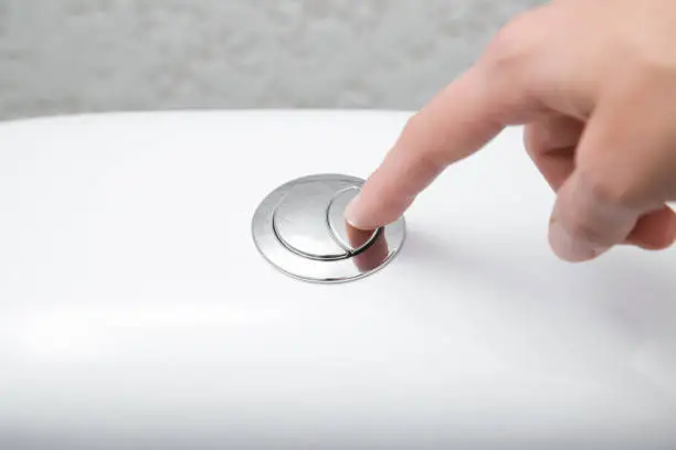 Photo of Young woman hand finger pushing button in toilet. Closeup.