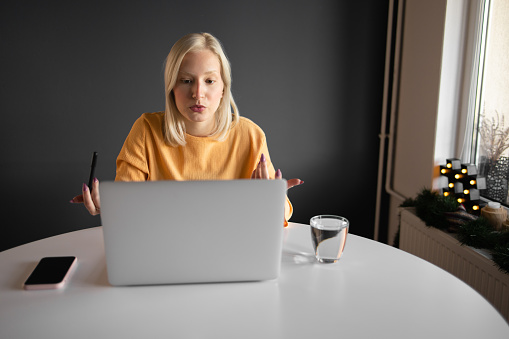 A young woman is sitting comfortably while doing a freelance job from her living room and drinking coffee.