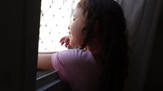 Little girl child looking outside through window, Small kid leaning on window peeking out