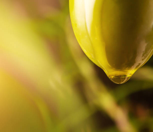 Drop of olive oil drips from green olive.