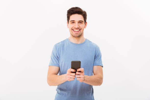 istock Happy man 30s in casual t-shirt typing sms or browsing internet using mobile phone, isolated over white background 1285112588