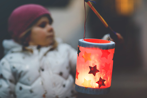 Close-up of little kid girl holding selfmade lanterns with candle for St. Martin procession. Healthy toddler child happy about children and family parade in kindergarten. German tradition Martinsumzug.