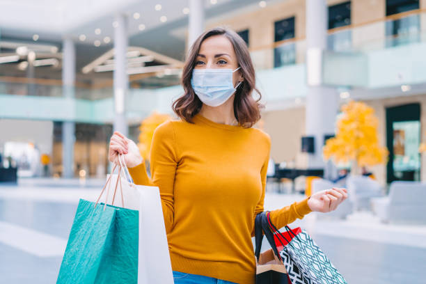 손에 쇼핑 가방의 무리와 쇼핑몰에서 산책하는 동안 보호 의료 마스크를 입고 캐주얼 옷을 입고 자신감 젊은 여성의 초상화 - mouth open retail shock surprise 뉴스 사진 이미지
