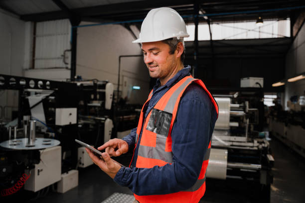 istock Smiling male engineer wearing uniform scrolling on tablet standing in factory 1285120182