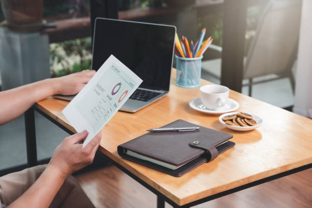 istock Young asian man holding document and working on laptop while sitting near window in home office. 1285120421