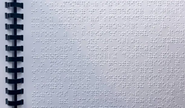 Close up of paper page with braille text. Visually impaired blind person learning to read by touch.