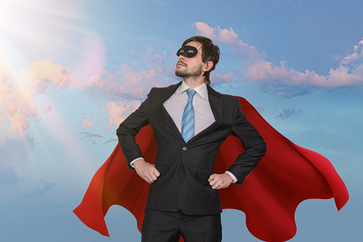 Funny brave businessman in suit as superhero. Sky in background.