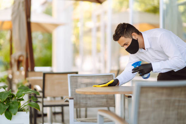 istock Young Waiter in protective face mask and gloves sanitizing surfaces. 1285123943