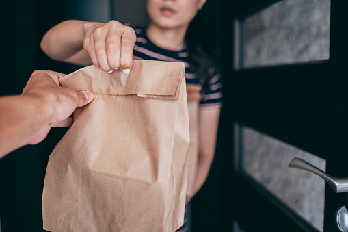 Woman holding paper bag with take out food, home delivery, food order