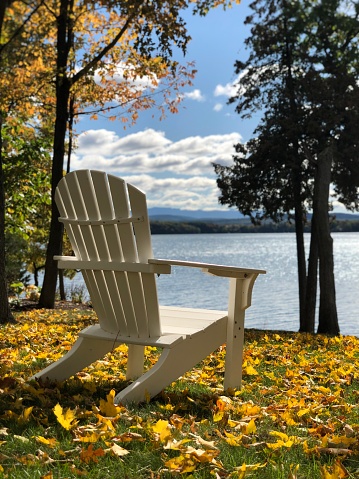 White Adirondack chair sitting near beautiful lake on an autumn day