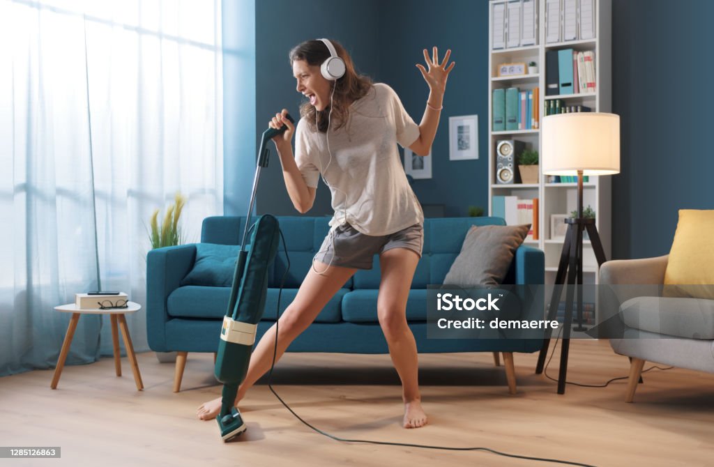 Woman cleaning up her house and singing Cheerful woman cleaning up her home and singing, she is using the vacuum cleaner as a microphone Dancing Stock Photo