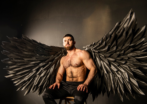 handsome physically well-developed man with black angel wings on a dark background