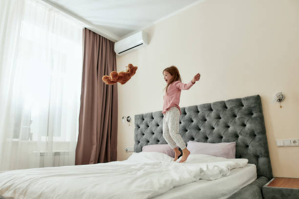 istock A cute girl having fun on a big bed throwing her teddybear up and jumping barefoot 1285128558