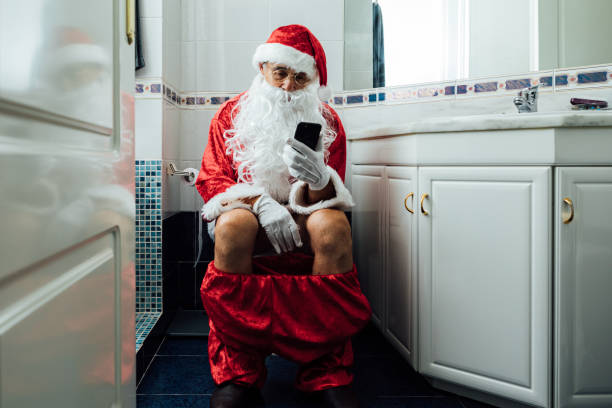 Santa Claus in the bathroom, sitting on the toilet pooping and looking at his cell phone stock photo