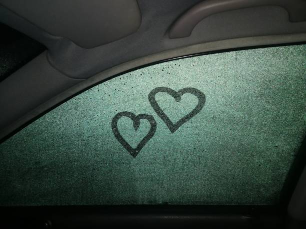 Painted two hearts on a dewy car window, view from inside, it's dark outside