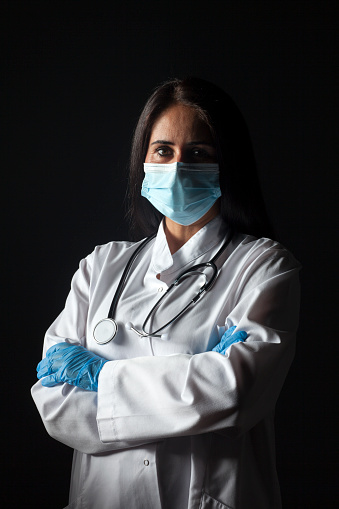 Female doctor wearing a disposable protective mask against covid-19 coronavirus infections on a black background